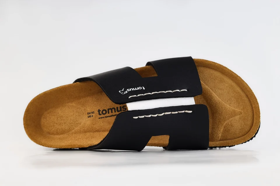 Close-up of the white stitching and Tomus branding on a black sandal